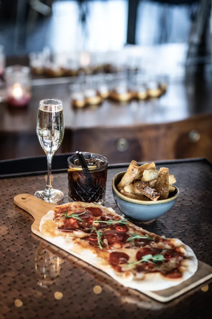 A pepperoni flatbread, chips and a glass of prosecco on a table at KWB