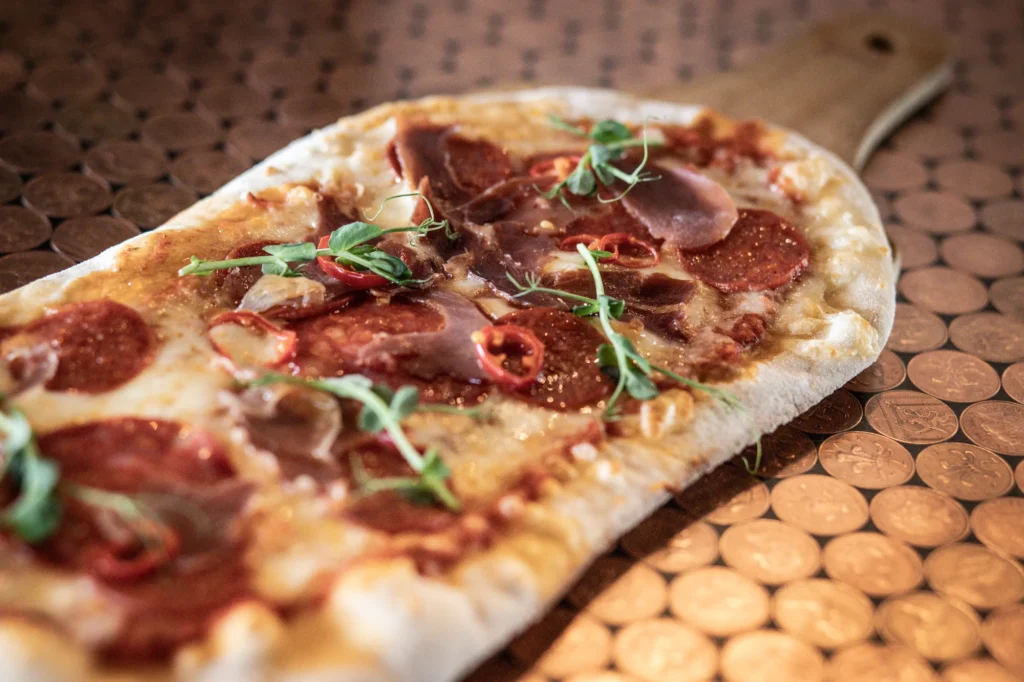 Close up of a pepperoni and rocket flatbread on a wooden board at KWB